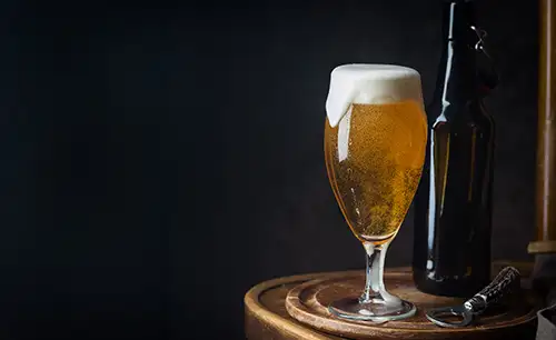 A glass of beer sitting on a table, against a dark background